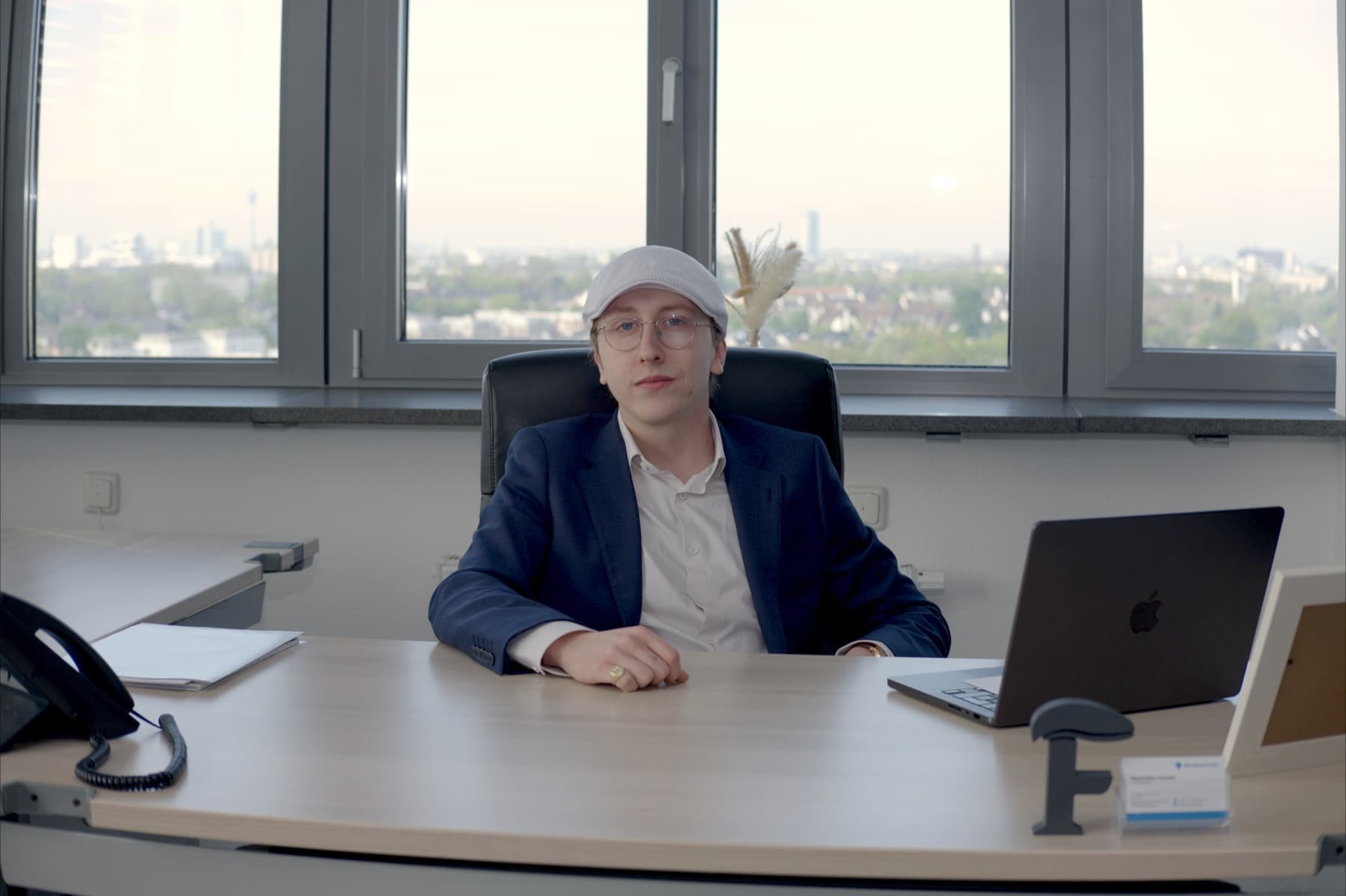 Maximilian Fanslau at his desk in the Düsseldorf office, with the city skyline behind him