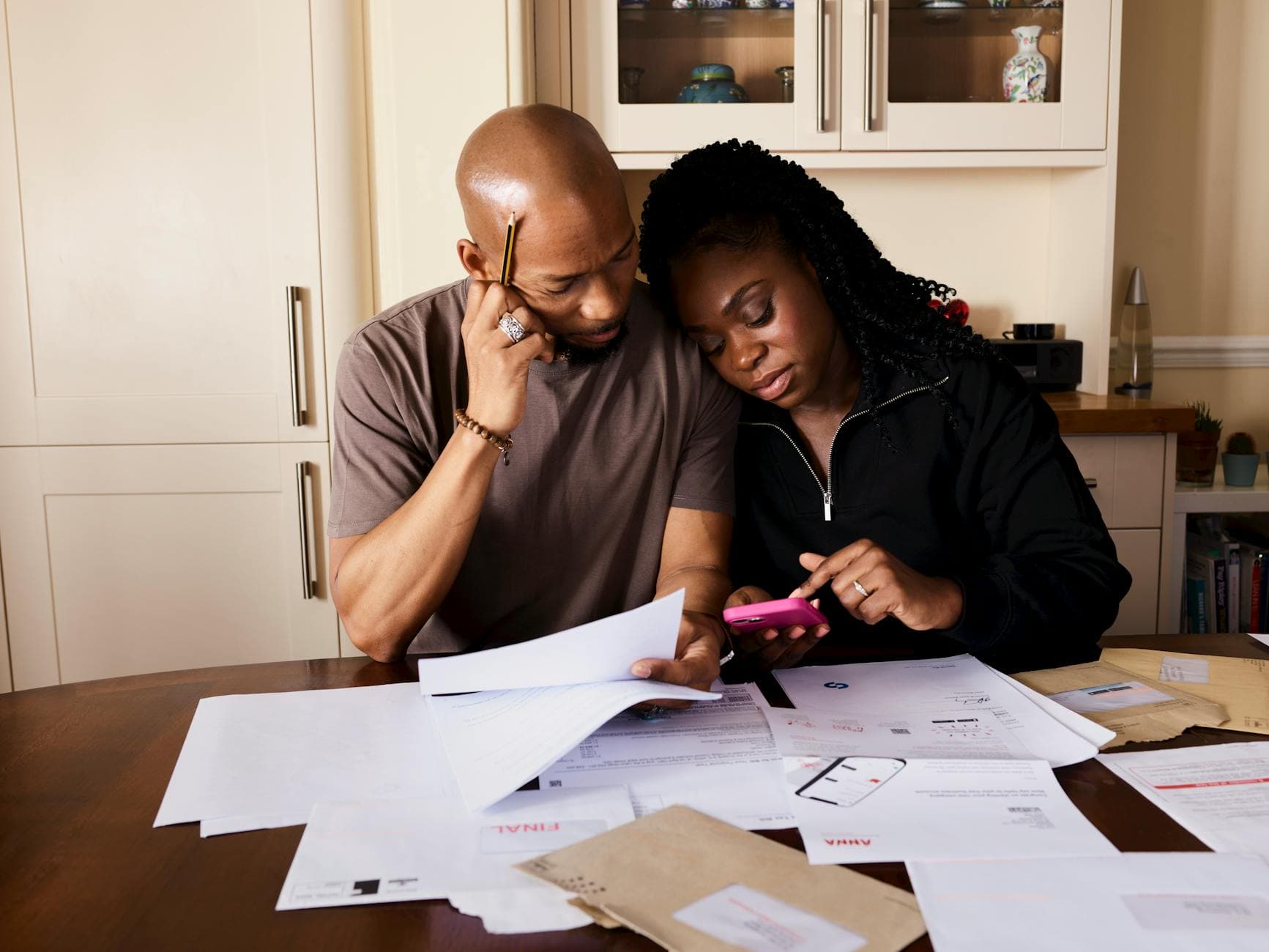 A couple sits at a table managing domestic finances, evaluating documents and using a smartphone.