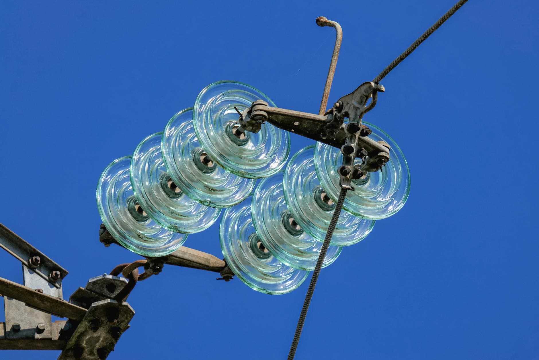 Close-up of a high voltage glass insulator suspended against a bright blue sky, reflecting modern electrical technology.
